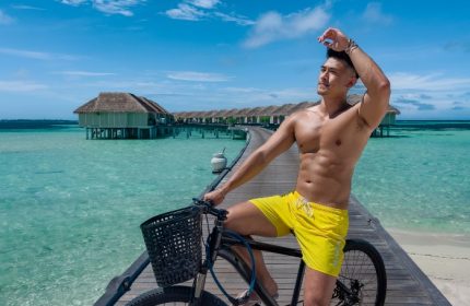 Gay travel: LUX* South Ari Atoll, Maldives. Man on bike, yellow shorts. Top staff friendly hotel, overwater bungalows. Paradise.