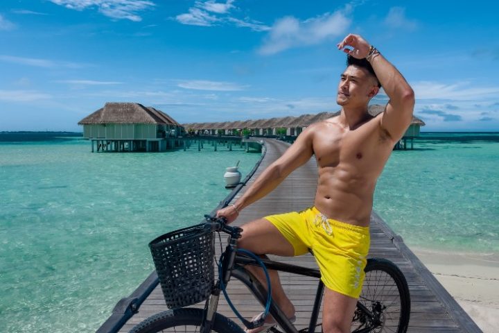 Gay travel: LUX* South Ari Atoll, Maldives. Man on bike, yellow shorts. Top staff friendly hotel, overwater bungalows. Paradise.