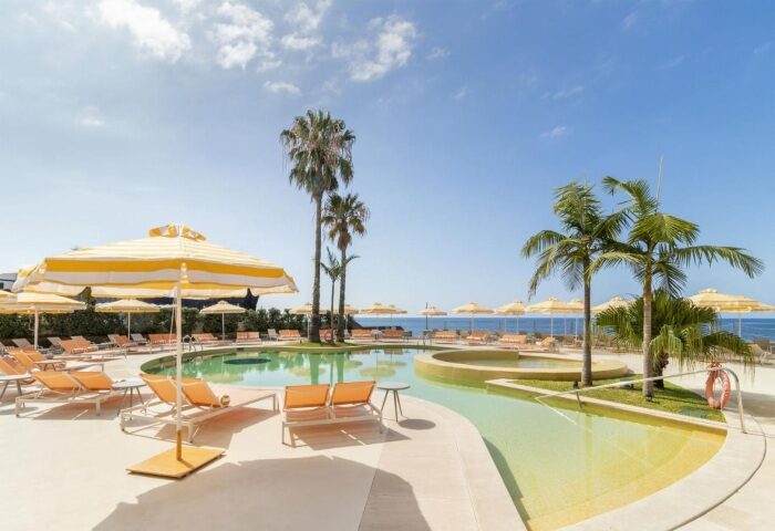 NEXT Hotel Madeira pool view. Gay beach resort in Portugal with palm trees, sun loungers, and yellow umbrellas. Top gay travel destination.