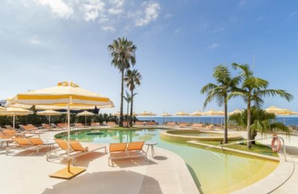 NEXT Hotel Madeira pool view. Gay beach resort in Portugal with palm trees, sun loungers, and yellow umbrellas. Top gay travel destination.