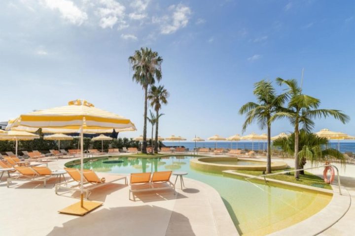 NEXT Hotel Madeira pool view. Gay beach resort in Portugal with palm trees, sun loungers, and yellow umbrellas. Top gay travel destination.