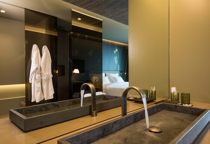 Saccharum Hotel Madeira bathroom with modern sinks, robes, and a mirror reflecting the bed. Top honeymoon beach hotel for mister and mister travel.