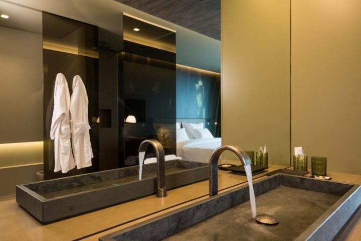 Saccharum Hotel Madeira bathroom with modern sinks, robes, and a mirror reflecting the bed. Top honeymoon beach hotel for mister and mister travel.