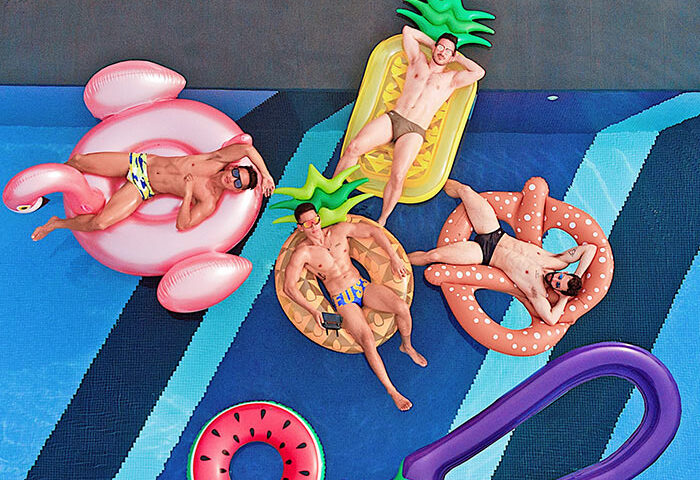 Koh Samui gay beach destination: Men relax on inflatables in a pool. Thailand travel for gay men. Pool party, summer vibes.