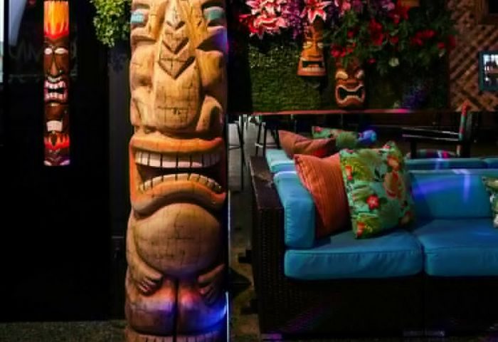 Toucans Tiki Lounge: Gay bar interior with tiki statues, floral decorations, and comfy blue sofas. A fun, tropical experience.