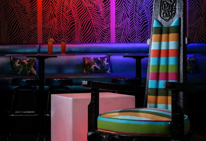 Toucans Tiki Lounge interior. Gay bar seating area with colorful striped chair, tropical wallpaper, and drinks. Gay travel destination.