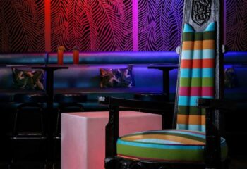 Toucans Tiki Lounge interior. Gay bar seating area with colorful striped chair, tropical wallpaper, and drinks. Gay travel destination.