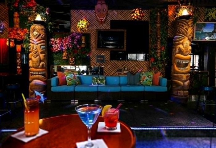 Toucans Tiki Lounge interior. Gay bar with tiki statues, bamboo wall, blue sofa, and tropical cocktails. Gay travel destination.