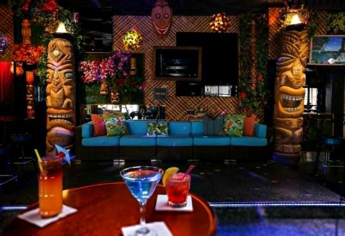 Toucans Tiki Lounge interior. Gay bar with tiki statues, bamboo wall, blue sofa, and tropical cocktails. Gay travel destination.