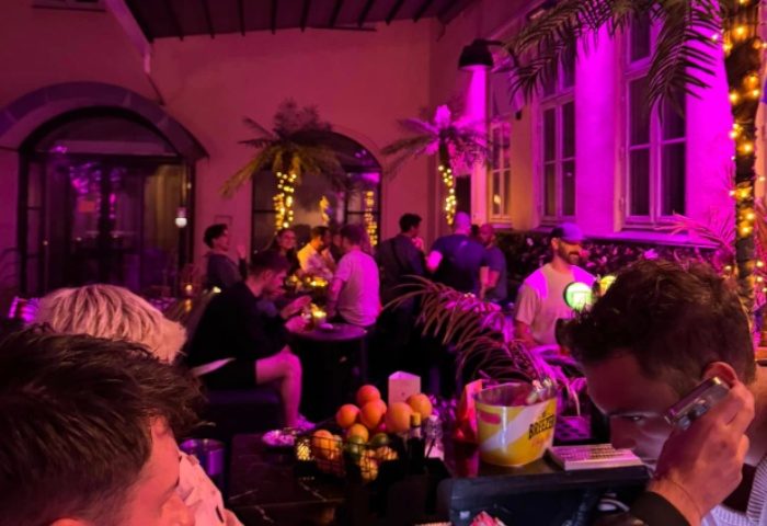 Trixie Copenhagen: Gay bar scene with men socializing under purple lights and palm trees. A vibrant nightlife spot for gay travel.