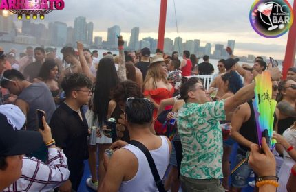 Crowd at True Colors Bar in New York City. Gay men and women party with drinks. NYC skyline visible. Gay travel destination.