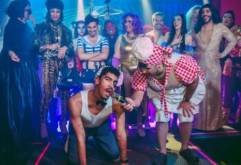 Lisbon's Trumps gay bar: a diverse group poses, including drag queens and a man on all fours being interviewed. Gay travel nightlife.