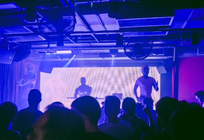 Lisbon gay nightlife: Crowd at Trumps gay club. DJ and dancers perform on stage with blue lighting. Gay travel advice for Lisbon, Portugal.