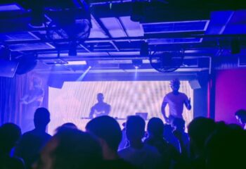 Lisbon gay nightlife: Crowd at Trumps gay club. DJ and dancers perform on stage with blue lighting. Gay travel advice for Lisbon, Portugal.