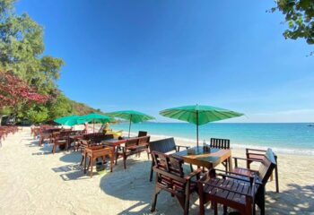Tub Tim Resort's beach vibe in Koh Samet. Tables with umbrellas on white sand beach, turquoise water, blue sky. Best gay beach.