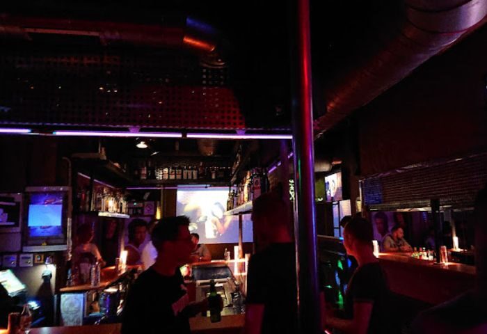 Interior of Tubos Gay Bar in Gran Canaria. People at the bar, drinks, and a projector screen. Nightlife scene. Gay travel advice.