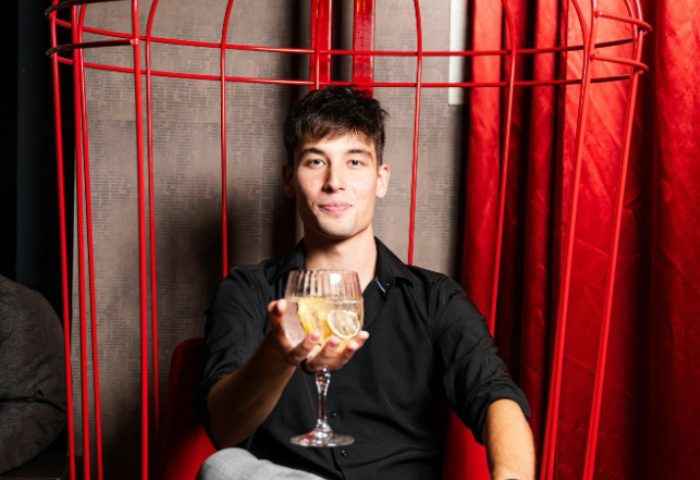 Gay man at Tuk Tuk Bar, Budapest. He's holding a drink in a red cage chair. Nightlife in Budapest's gay scene.