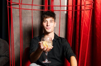 Gay man at Tuk Tuk Bar, Budapest. He's holding a drink in a red cage chair. Nightlife in Budapest's gay scene.
