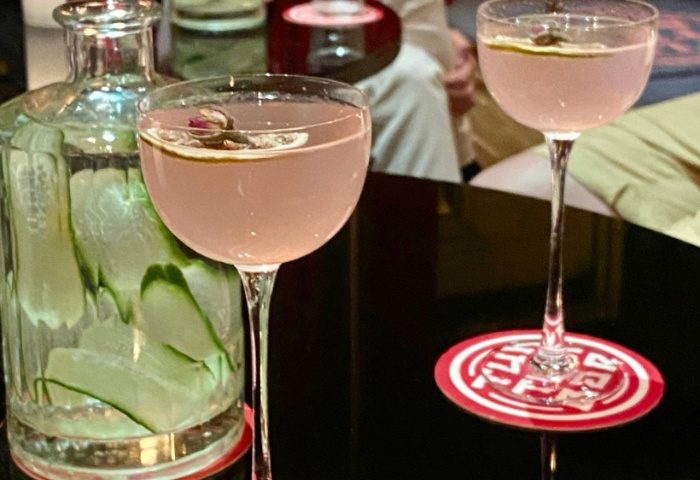 Cocktails at Tuk Tuk Bar, Budapest. Pink drink in stemmed glass with garnish. Bottle with cucumber slices. Gay travel advice.