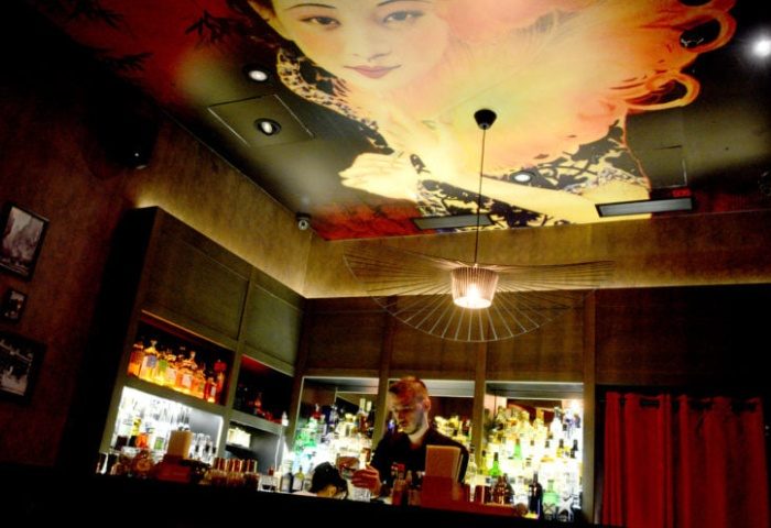 Tuk Tuk Bar, Budapest. Bartender at work in a stylish, dimly lit bar with a large Asian-themed mural on the ceiling. Gay travel advice.