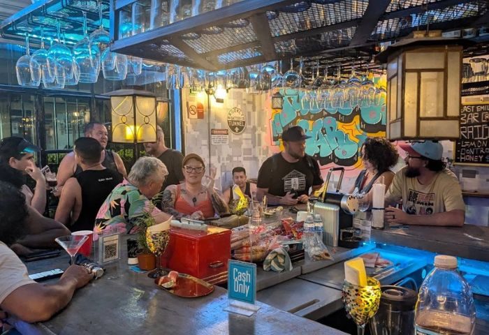 Patrons at Tunnel Gay Bar in Puerto Vallarta. People drink & chat at the bar, glasses hang above. Gay travel advice, nightlife scene.
