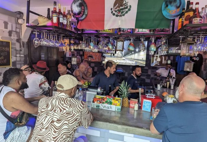 Inside Tunnel Gay Bar in Puerto Vallarta, Mexico. People at the bar, Mexican flag, bottles, and glasses. Gay travel destination.