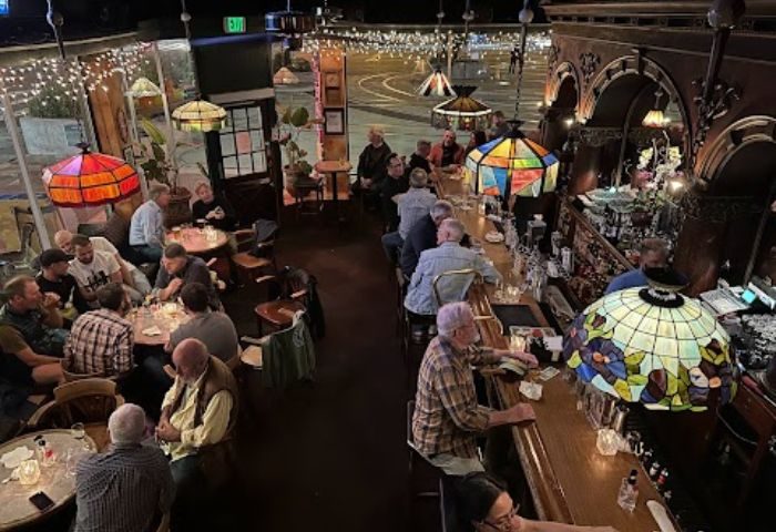 Twin Peaks Tavern in San Francisco, a historic gay bar, is filled with patrons at tables and the bar. Stained glass lamps add charm.