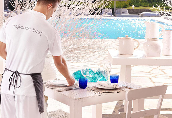 Mykonos Bay Resort & Villas: Waiter setting table with typical Mykonos design near the beach. Gay beachfront hotel with pool view.