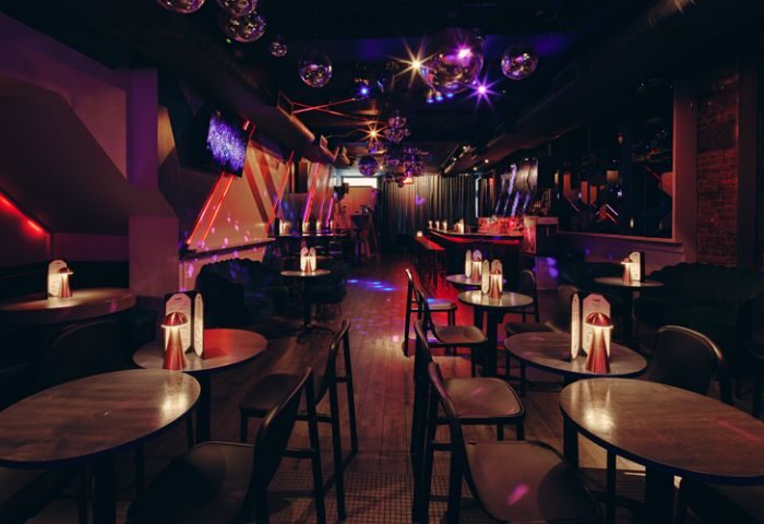 Interior of VERS, a gay venue in New York. Tables, chairs, bar, disco balls, and colorful lighting create a vibrant atmosphere. Nightlife travel.
