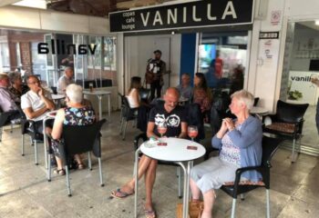 Vanilla Cafe Gay Bar in Torremolinos: Patrons at outdoor tables, musician playing guitar. A popular gay-friendly spot for drinks and socializing.