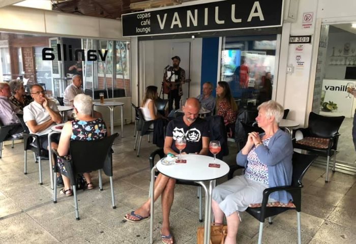 Vanilla Cafe Gay Bar in Torremolinos: Patrons at outdoor tables, musician playing guitar. A popular gay-friendly spot for drinks and socializing.