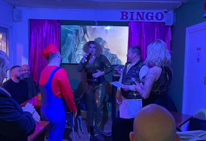 Vanilla Cafe gay bar in Torremolinos: drag queen performing bingo, man in Mario costume, and audience enjoying the show. Gay travel.