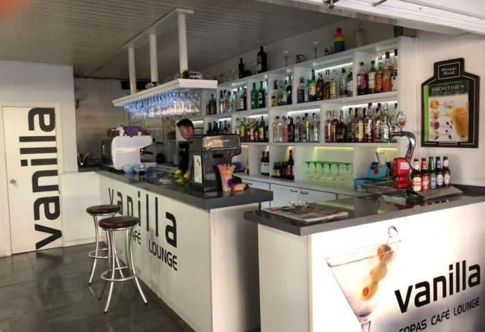 Vanilla Cafe Gay Bar in Torremolinos: Interior view of the bar area, showing bar stools, liquor shelves, and a bartender. Gay travel advice.