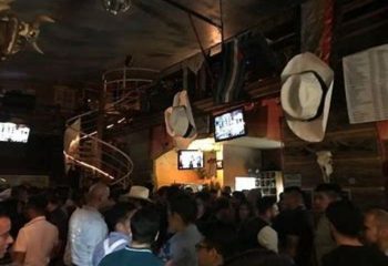 Inside Vaqueros Gay Bar in Mexico, a crowded space with cowboy hats hanging from the ceiling & a spiral staircase, for gay men travel advice.