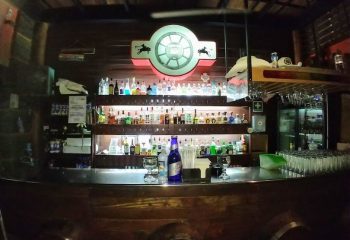 Inside Vaqueros Gay Bar in Mexico: A fully stocked bar with bottles, glasses, and a neon sign. Gay travel destination.