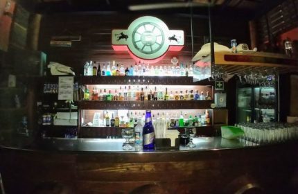 Inside Vaqueros Gay Bar in Mexico: A fully stocked bar with bottles, glasses, and a neon sign. Gay travel destination.