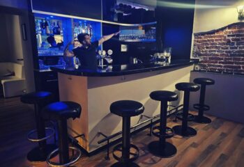 Vienna Schick Bar interior: Bartender gesturing behind the bar with stools. Gay bar in Vienna, perfect for gay men travel advice.