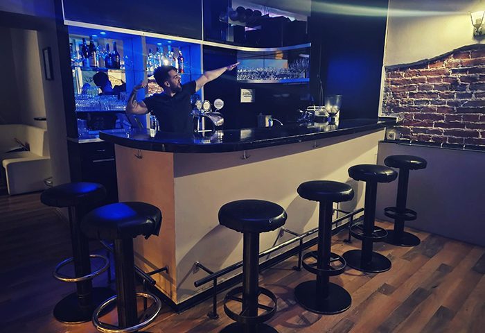 Vienna Schick Bar interior: Bartender gesturing behind the bar with stools. Gay bar in Vienna, perfect for gay men travel advice.