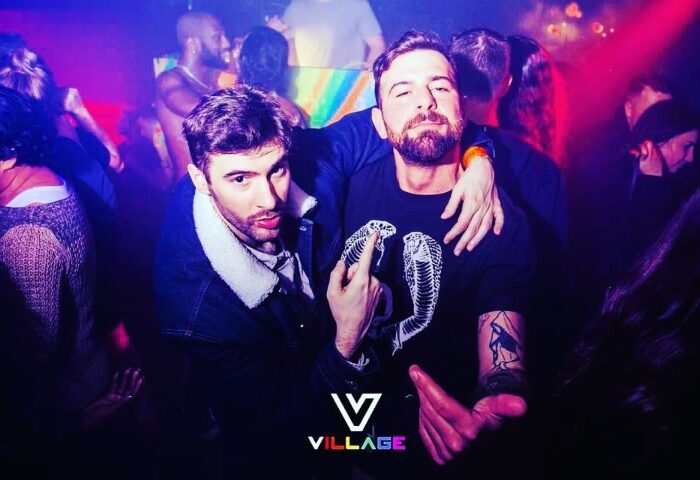 Two men at Village Soho, London's coolest gay bar. Nightlife scene with go-go boys. Fun times at this gay travel destination.