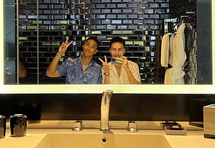 Gay couple selfie at W Bangkok, a top gay hotel in Silom, Bangkok. Two men pose in the bathroom mirror, peace signs up, enjoying their stay.