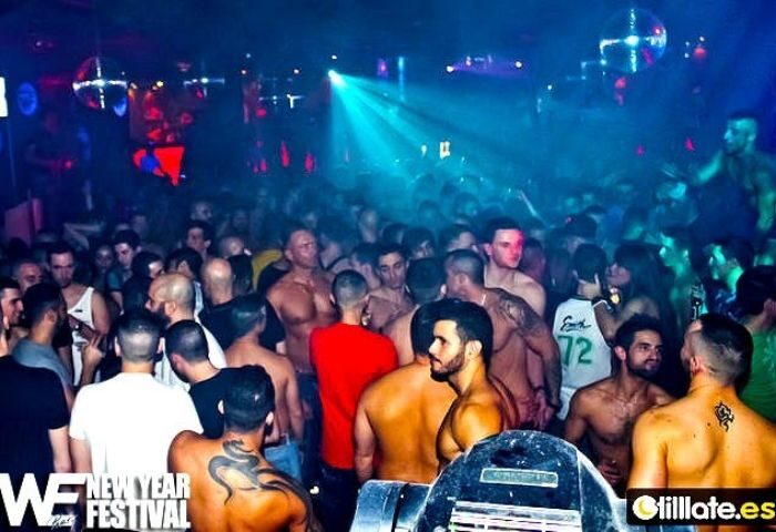 Crowded WE Party Madrid gay bar. Shirtless men, disco balls, and blue lighting create a vibrant atmosphere. Gay nightlife in Madrid.