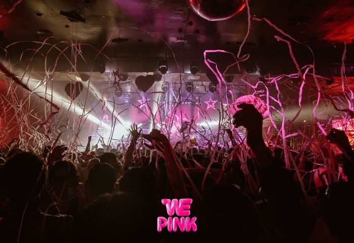Crowd at WE Party, a gay bar in Madrid, Spain. Confetti falls as people dance under pink lights and a disco ball.