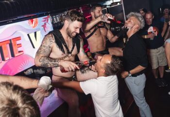 Gay men at WHY NOT Vienna. Leather-clad bartenders pour shots. Nightlife scene, travel advice. Gay bar in Vienna, Austria. Fun, party.