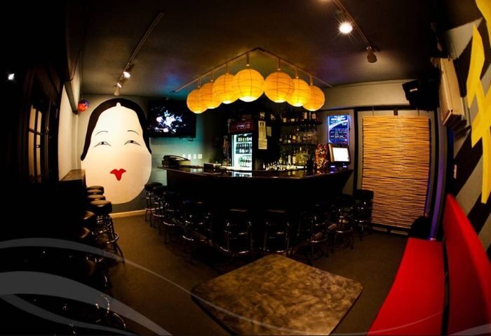 Wang Chung's Karaoke Bar interior in Honolulu. Asian-themed decor, bar with stools, and a large geisha face mural. Drinks and gay travel.