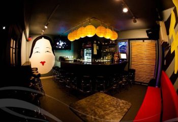 Wang Chung's Karaoke Bar interior in Honolulu. Asian-themed decor, bar with stools, and a large geisha face mural. Drinks and gay travel.