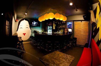 Wang Chung's Karaoke Bar interior in Honolulu. Asian-themed decor, bar with stools, and a large geisha face mural. Drinks and gay travel.