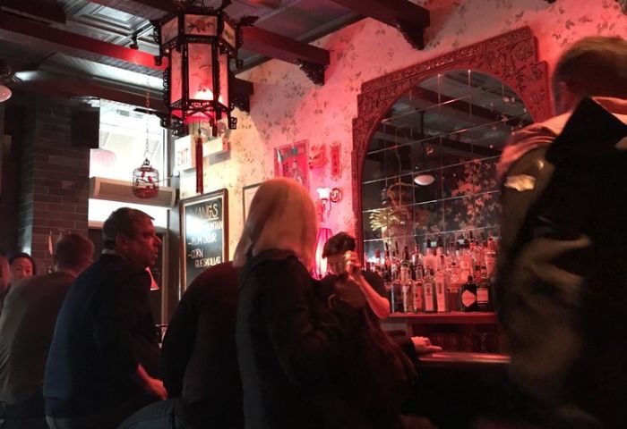Inside Wang's gay bar in Chicago. Patrons sit at the bar, red lighting, ornate mirror, and Asian-inspired decor. Gay travel destination.