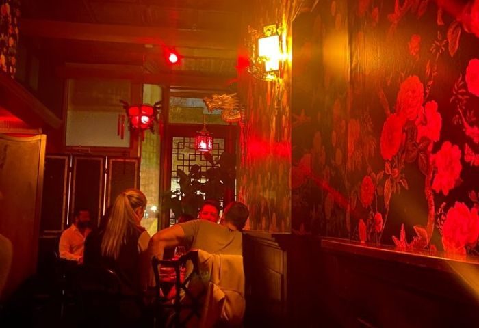 Interior of Wangs gay bar in Chicago. Red lighting, floral wallpaper, and people seated at tables create a vibrant, intimate atmosphere.