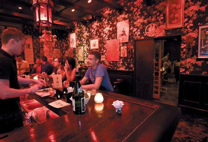 Inside Wangs Gay Bar in Chicago. Bartender, patrons at bar. Floral wallpaper, Asian decor, red lighting. Gay travel advice.