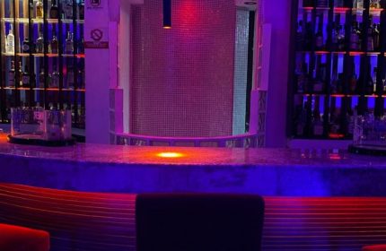 Wet gay bar in Puerto Vallarta, Mexico. Bar counter with bottles, colorful lights, & a unique tiled backdrop for gay men travelers.